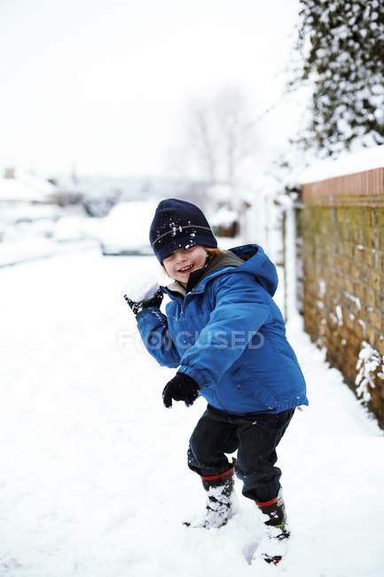 Хлопчик початкового віку в зимовому одязі грає на вулиці зі сніжкою . — стокове фото