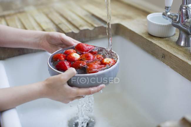 Vista cortada de menina lavando morangos frescos na pia . — Fotografia de Stock