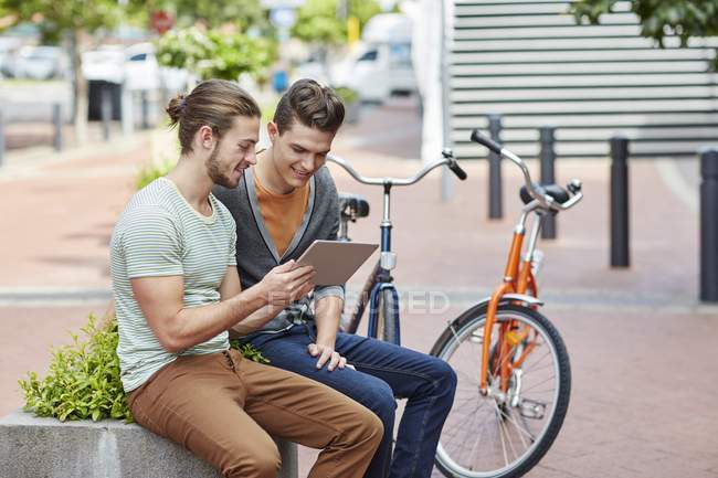 Jeunes hommes assis sur le mur de la rue avec tablette numérique . — Photo de stock