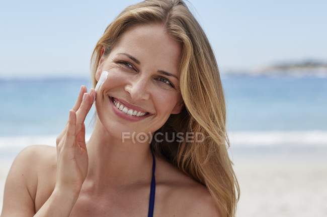 Mulher aplicando protetor solar na praia . — Fotografia de Stock