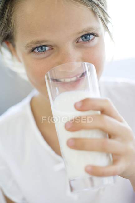 Età elementare ragazza bere latte da vetro . — Foto stock