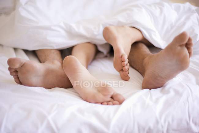 Un par de pies asomándose desde debajo del edredón en la cama . - foto de stock