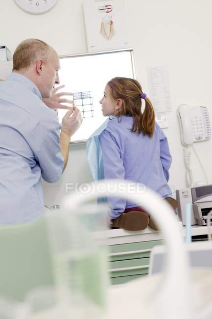 Zahnarzt hält Röntgenbild gegen Leuchtkasten und zeigt es Mädchen. — Stockfoto