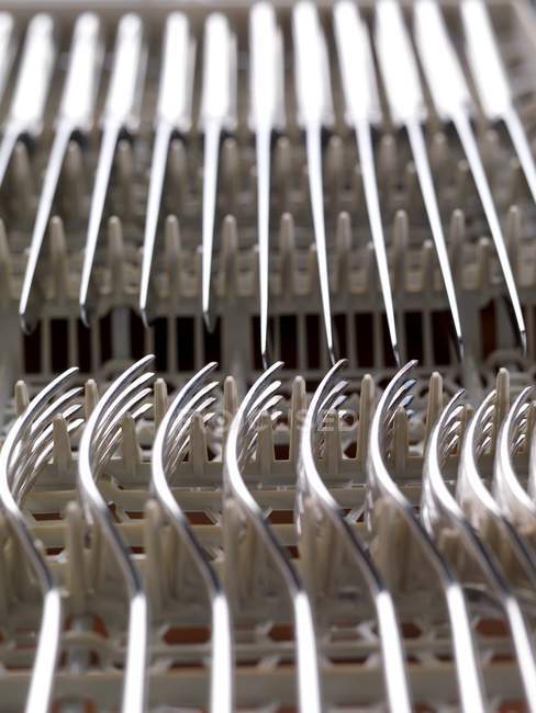 Cuchillos y tenedores limpios apilados en lavavajillas . - foto de stock