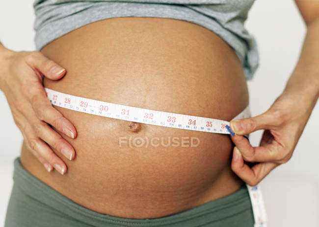 Vista recortada de la mujer embarazada que mide el abdomen hinchado . - foto de stock
