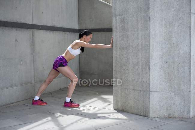 Young woman stretching against wall — Stock Photo