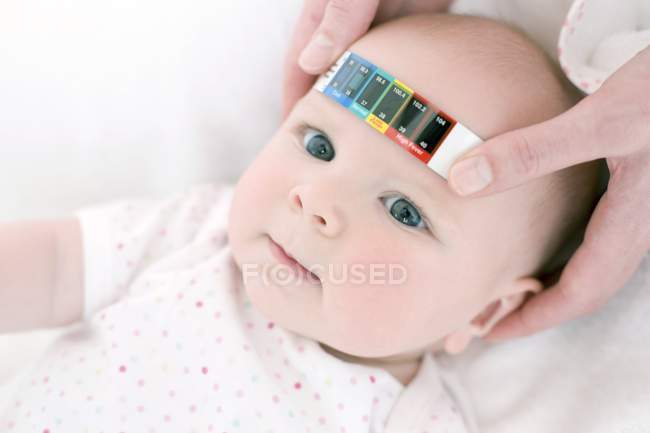 Mani femminili con termometro a strisce per misurare la temperatura del bambino . — Foto stock