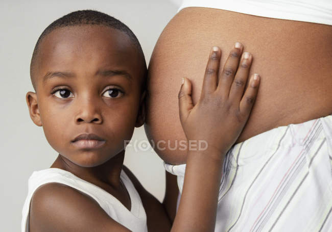 Niño en edad preescolar escuchando el abdomen hinchado de la madre embarazada . - foto de stock