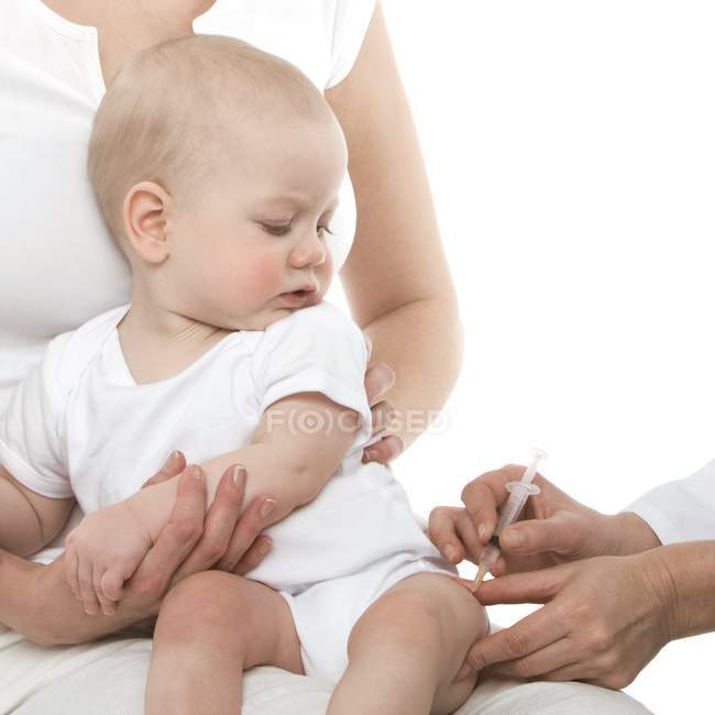 Vue recadrée de l'infirmière faisant la vaccination au bébé entre les mains de la mère . — Photo de stock