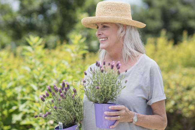 Старшая женщина держит горшки с растениями и улыбается . — стоковое фото