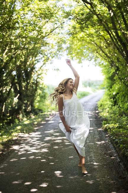 Donna in abito bianco che balla sulla strada di campagna . — Foto stock
