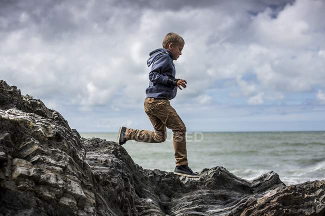 Menino da idade elementar correndo em rochas na praia . — Fotografia de Stock