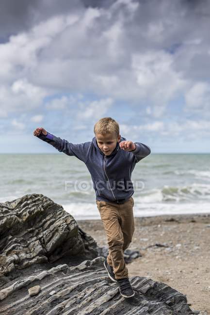Junge im Grundschulalter rennt am Strand auf Felsen. — Stockfoto