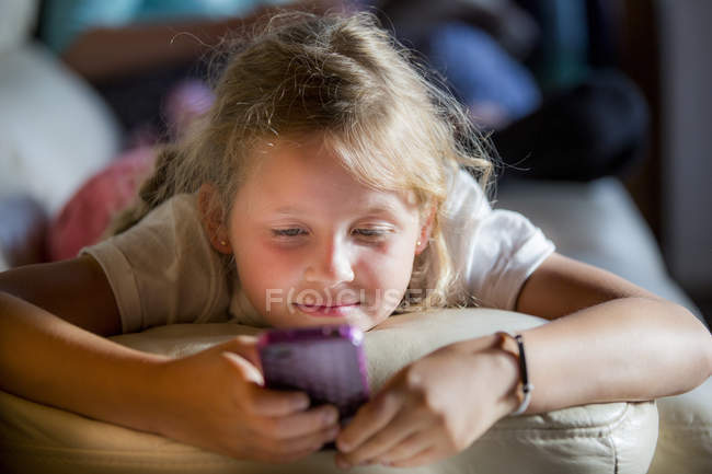 Mädchen liegt auf dem Sofa und benutzt Smartphone. — Stockfoto