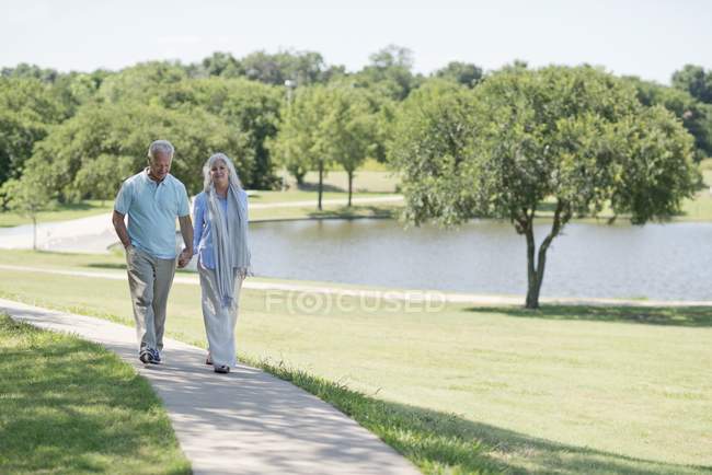 Couple sénior marchant sur le sentier dans le parc au bord du lac . — Photo de stock