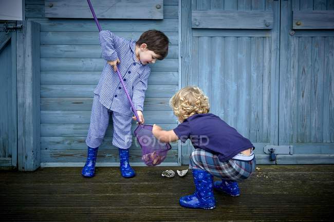 Two boys collecting seashells in fishing net in front of beach hut. — Stock Photo