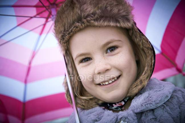 Portrait of preschooler girl wearing furry hat with pink umbrella. — Stock Photo