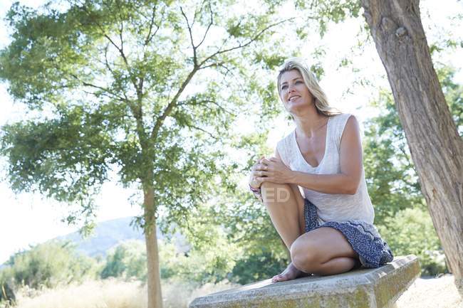 Mid adult woman sitting among park trees. — Stock Photo