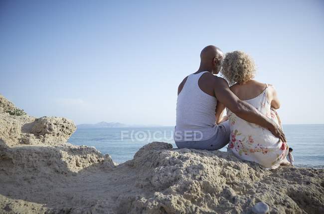 Пара сидить на скелі і дивиться в бік моря . — стокове фото