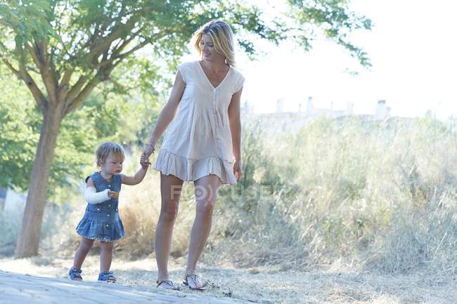 Mother and daughter with arm in plaster walking on park path. — Stock Photo