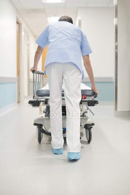 Enfermeira homem ordenadamente empurrando cama no corredor . — Fotografia de Stock