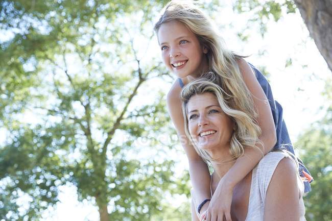 Mother carrying elementary age daughter on shoulders in park. — Stock Photo