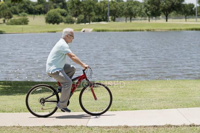 Homem sênior andar de bicicleta no parque, vista lateral . — Fotografia de Stock