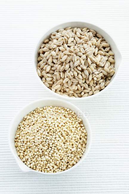Quinoa seeds and pearl barley in bowls. — Stock Photo