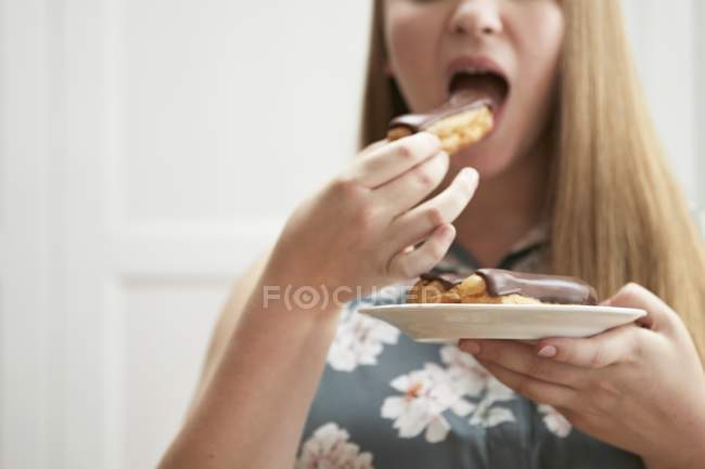 Jovem mulher comendo eclair chocolate — Fotografia de Stock
