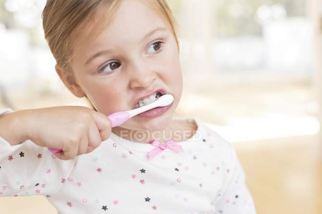 Elementary idade menina escovar os dentes e olhando para longe . — Fotografia de Stock