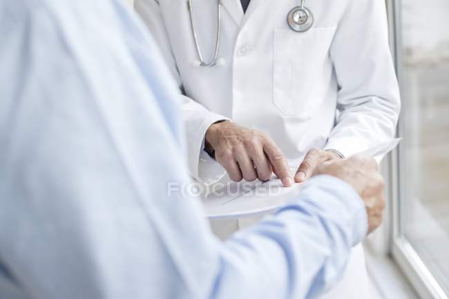 Male doctor pointing at medical notes with patient. — Stock Photo