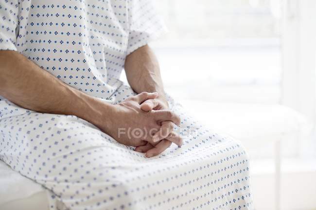 Paciente masculino usando bata de hospital y sentado en la cama . - foto de stock