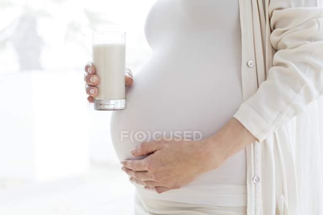 Mulher grávida com copo de leite tocando barriga . — Fotografia de Stock