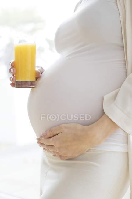 Mulher grávida com copo de suco de frutas tocando barriga
. — Fotografia de Stock