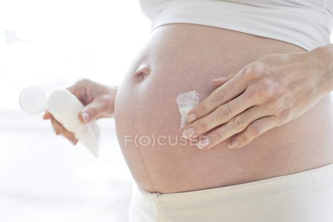 Беременная женщина увлажняет живот кремом — стоковое фото