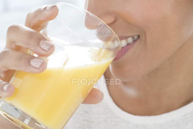 Femme adulte moyenne buvant un verre de jus d'orange, gros plan . — Photo de stock