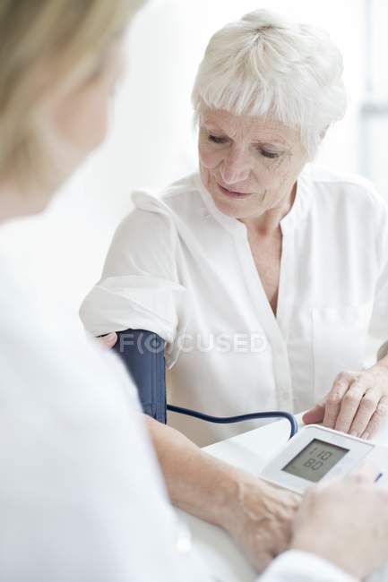 Médico femenino que toma la presión arterial de una mujer mayor . - foto de stock