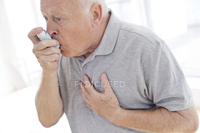 Senior man using inhaler while holding chest. — Stock Photo