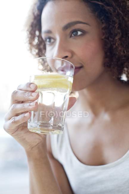 Жінка п'є воду зі шматочком лимона . — стокове фото