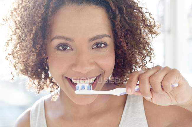 Mujer cepillándose los dientes y mirando a la cámara - foto de stock