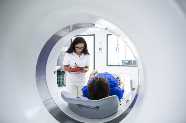 Radiólogo toma notas mientras paciente acostado en escáner CT . - foto de stock