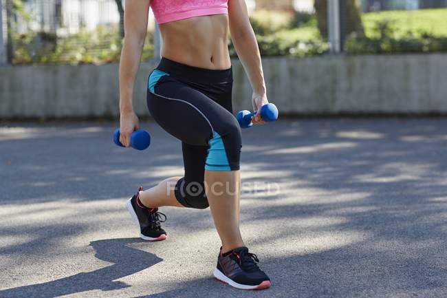 Young woman using weights while doing lunges. — Stock Photo