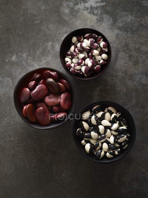 Beans in bowls on dark background, overhead view. — Stock Photo