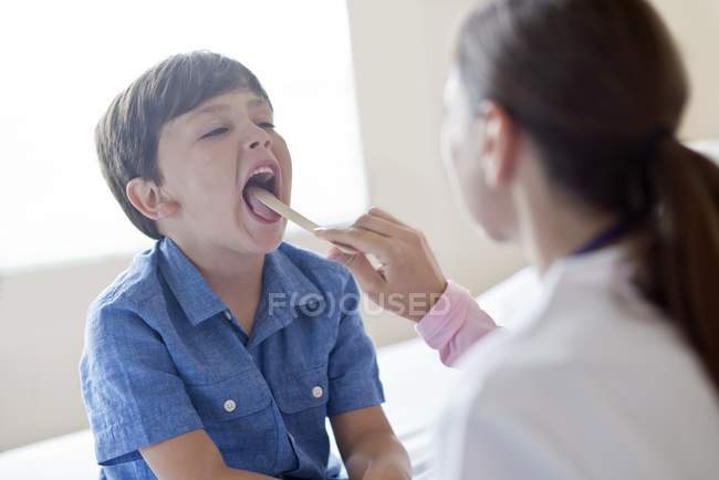 Female nurse using tongue depressor with boy. — Stock Photo