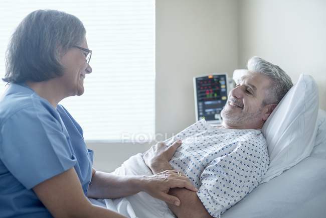 Enfermera sosteniendo mano de paciente masculino en cama de hospital . - foto de stock
