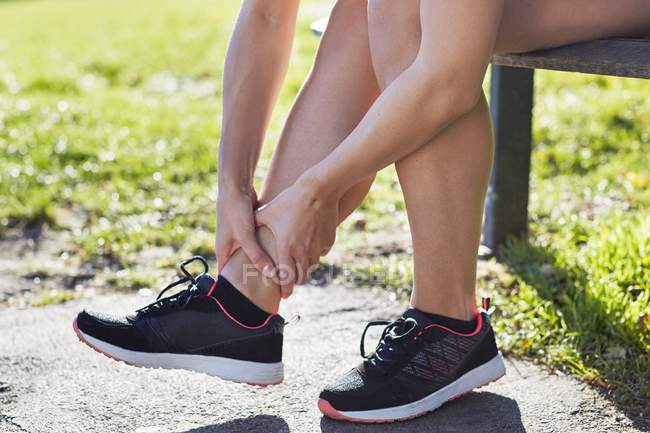 Woman wearing trainers holding ankle. — Stock Photo