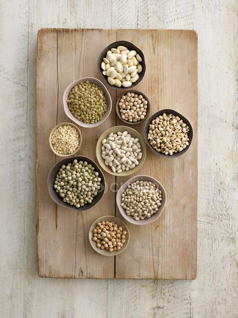 Legumes in bowls on chopping board, overhead view. — Stock Photo