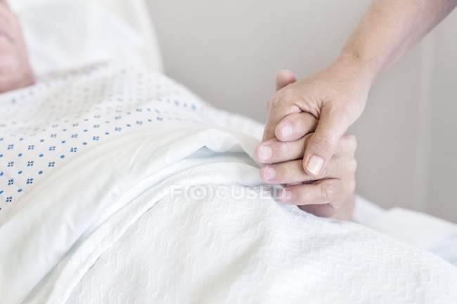 Enfermeira segurando a mão do paciente masculino na cama do hospital . — Fotografia de Stock
