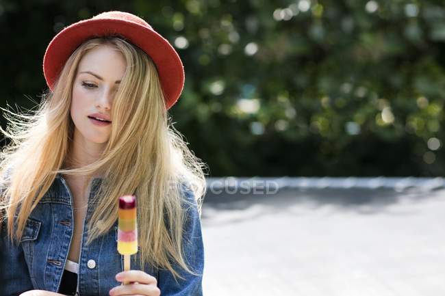 Young woman in red hat eating ice pop. — Stock Photo