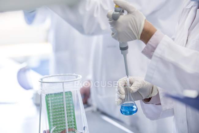 Scientist holding chemical flask and using pipette. — Stock Photo